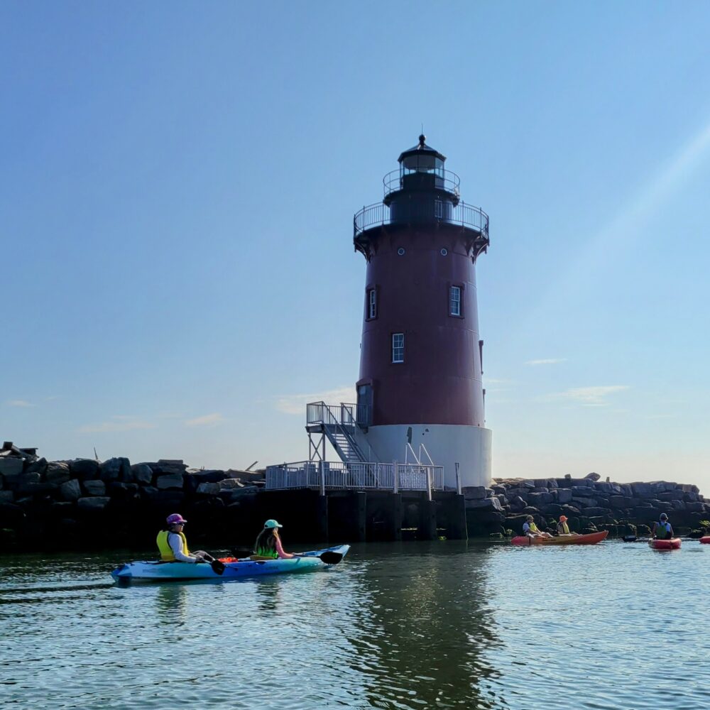 Kayaks on smooth water with lighthouse in the background.