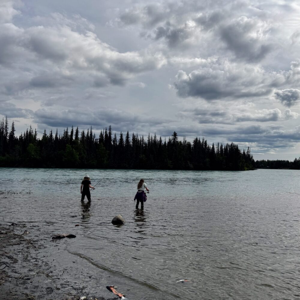 Two kids in waders fishing in a river.