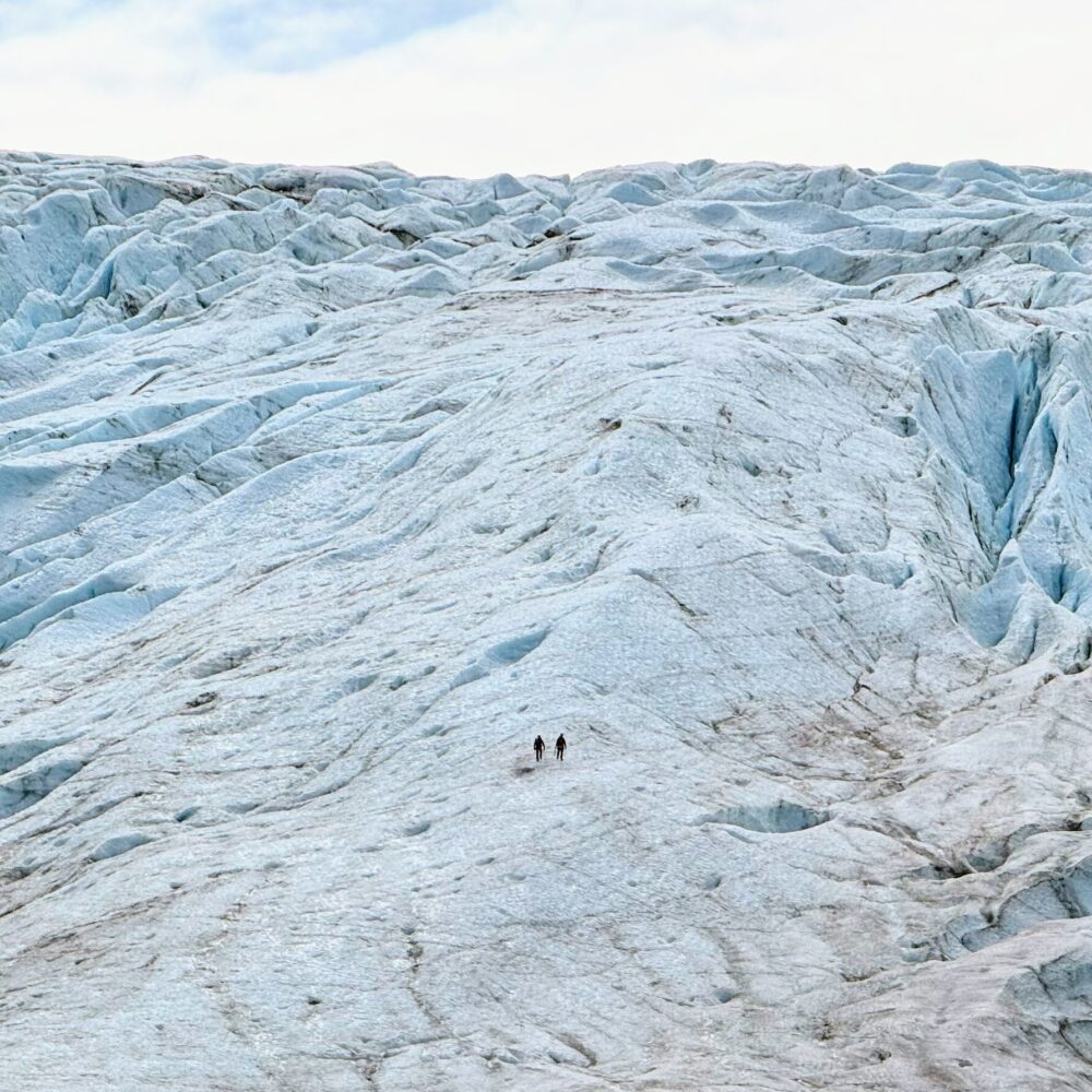 Two hikers looking very small on Portage Glacier. 